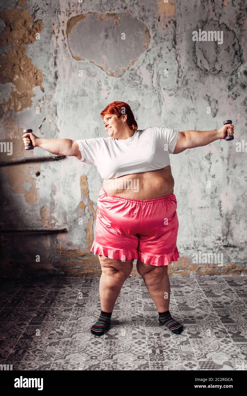 Grosse femme sur l'entraînement physique avec haltères courtes, lutte contre l'obésité, l'excès de poids. Manger de la restauration rapide Banque D'Images