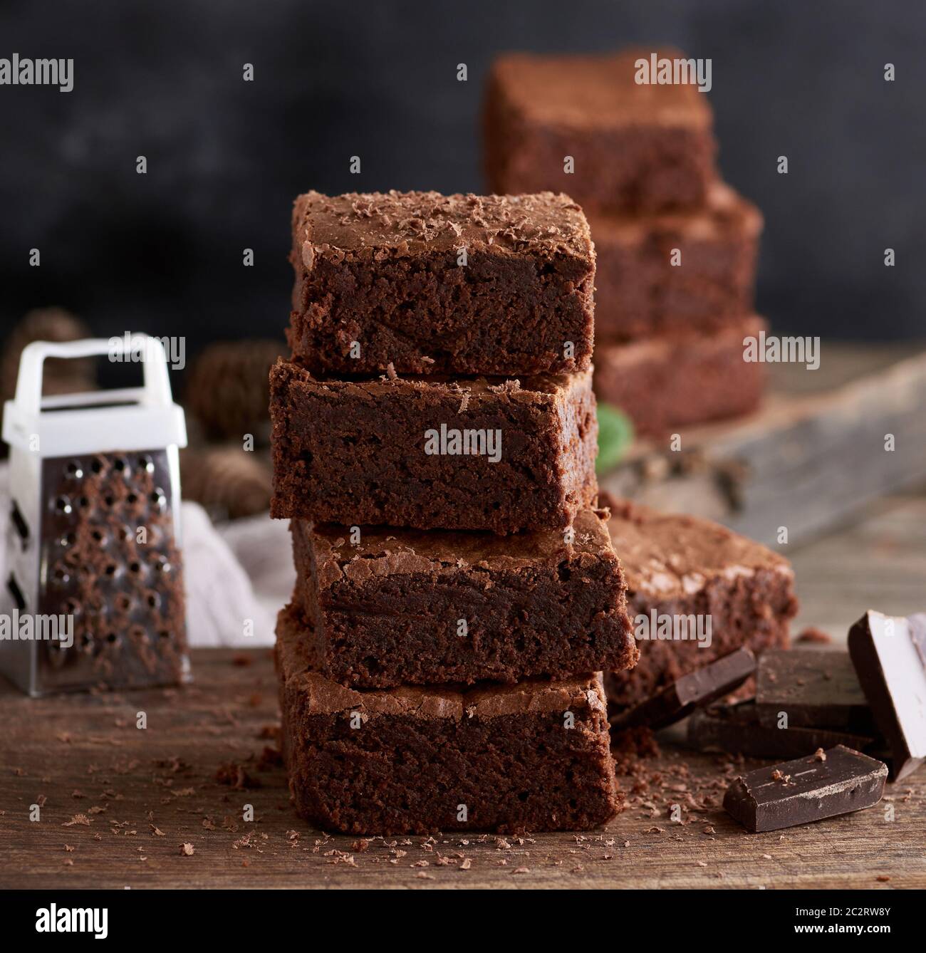 Pile de petits morceaux carrés de brownies gâteau sur une planche à découper en bois brun, fond noir Banque D'Images