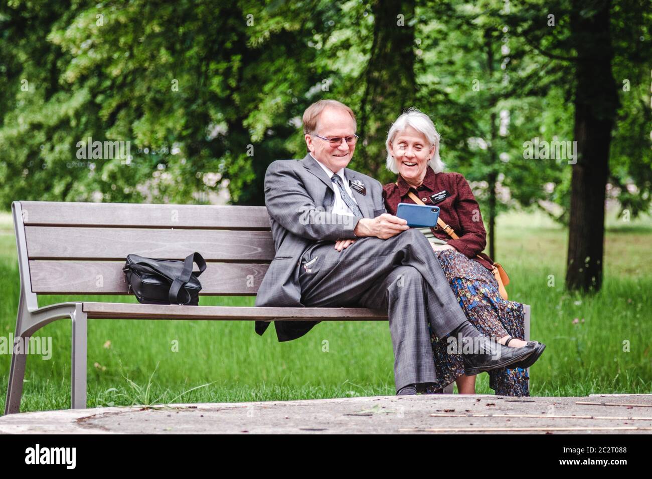 Heureux positif, un couple plus âgé riant et regardant le téléphone mobile sur banc au parc par beau temps Banque D'Images