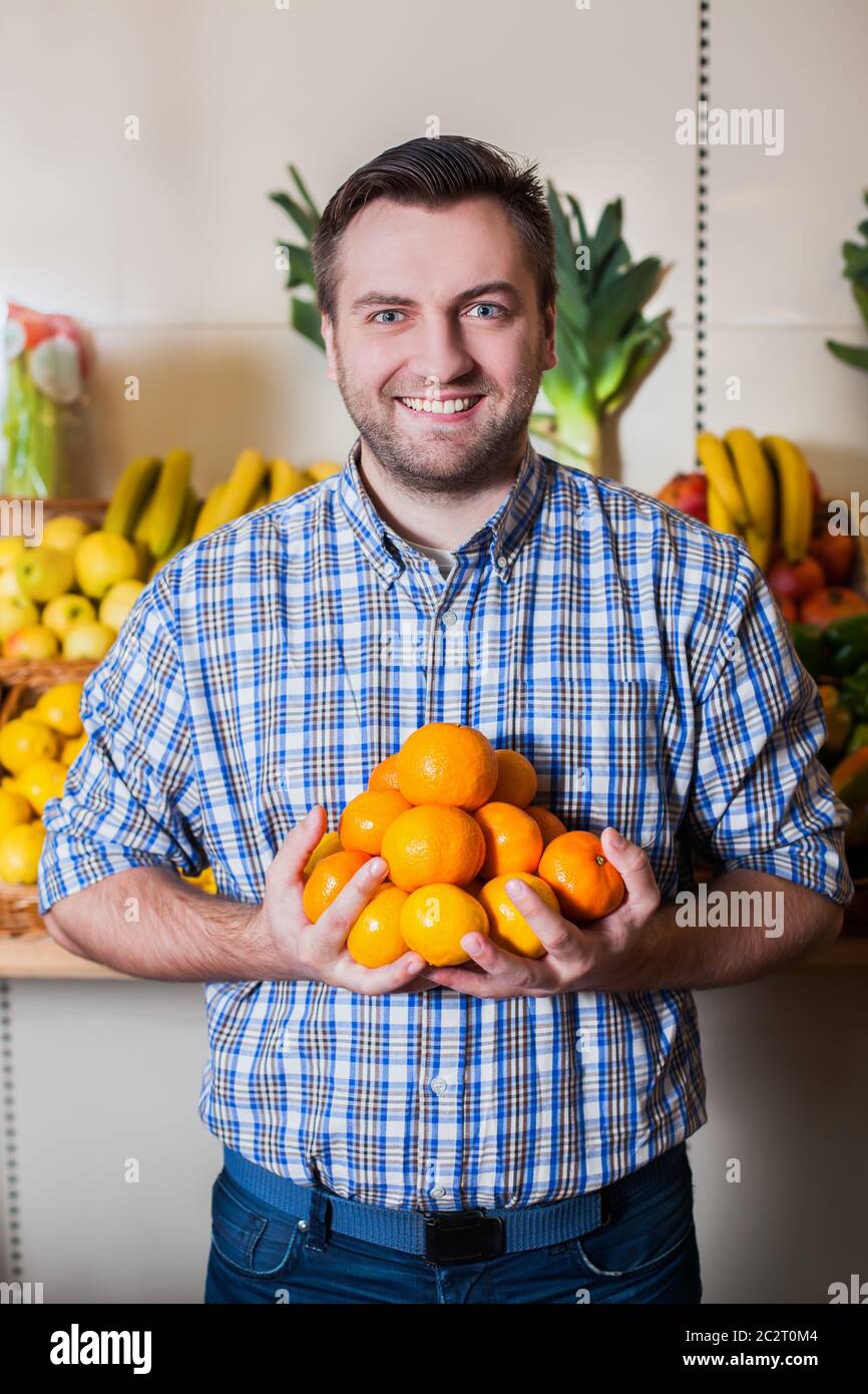 Portrait d'homme souriant tient des mandarines mûres entre les mains. Banque D'Images