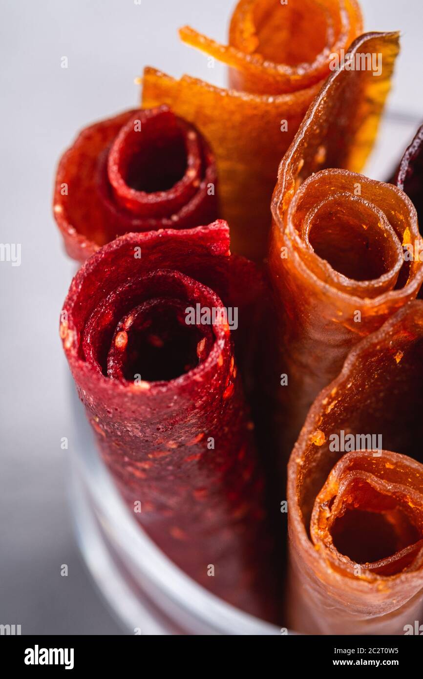 Pastille de fruits dans une tasse de verre sur fond de béton de pierre. Nourriture roulait sans sucre biologique à base de framboise, fraise, pêche et pomme. Maison végétalienne Banque D'Images