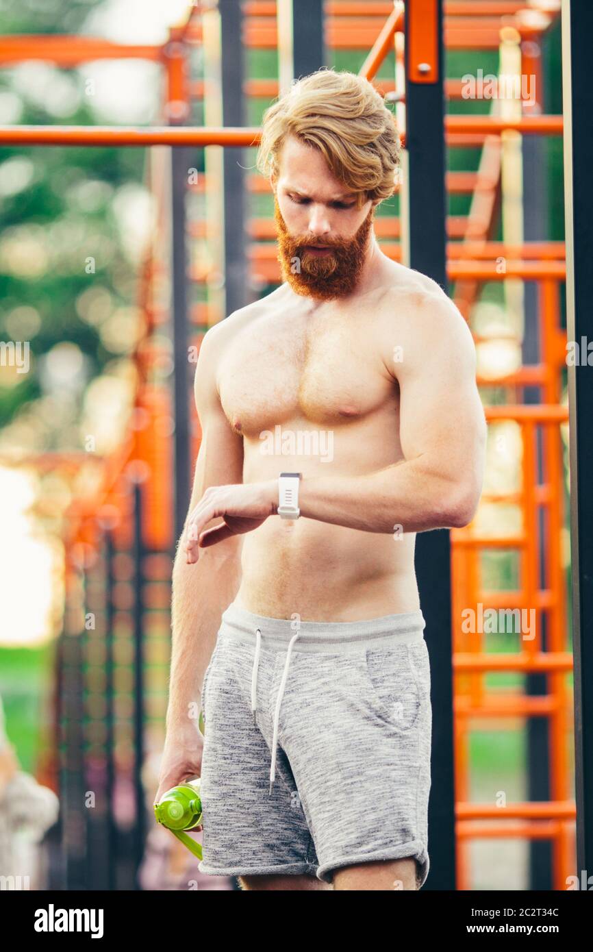 Sportif regardant la montre debout treet gym. Jeune athlète musclé vérifiant les résultats sportifs sur la montre intelligente après un bon entraînement Banque D'Images