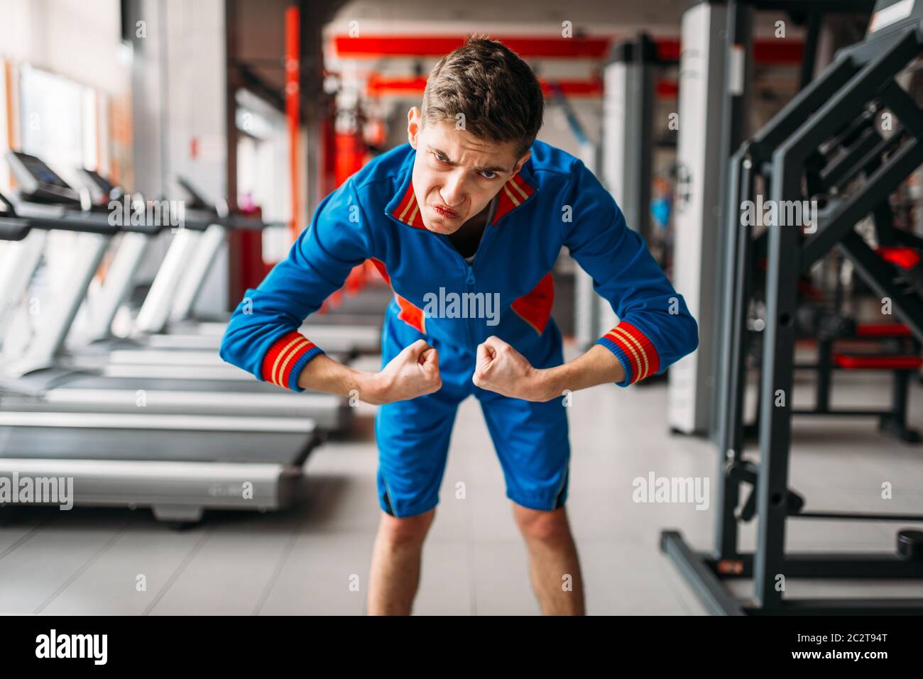 L'homme maigre dans les vêtements de sport montre ses muscles dans la salle  de sport, l'humour. Faible personne mâle dans le sport club Photo Stock -  Alamy