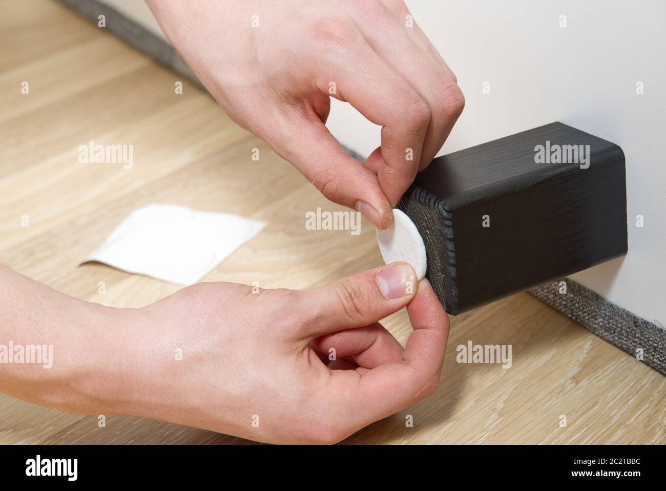 L'homme colle le coussin de soin du sol aux pieds en bois du lit. Couvre-coussin en feutre antidérapant à poser sur la jambe de meuble en bois. Banque D'Images