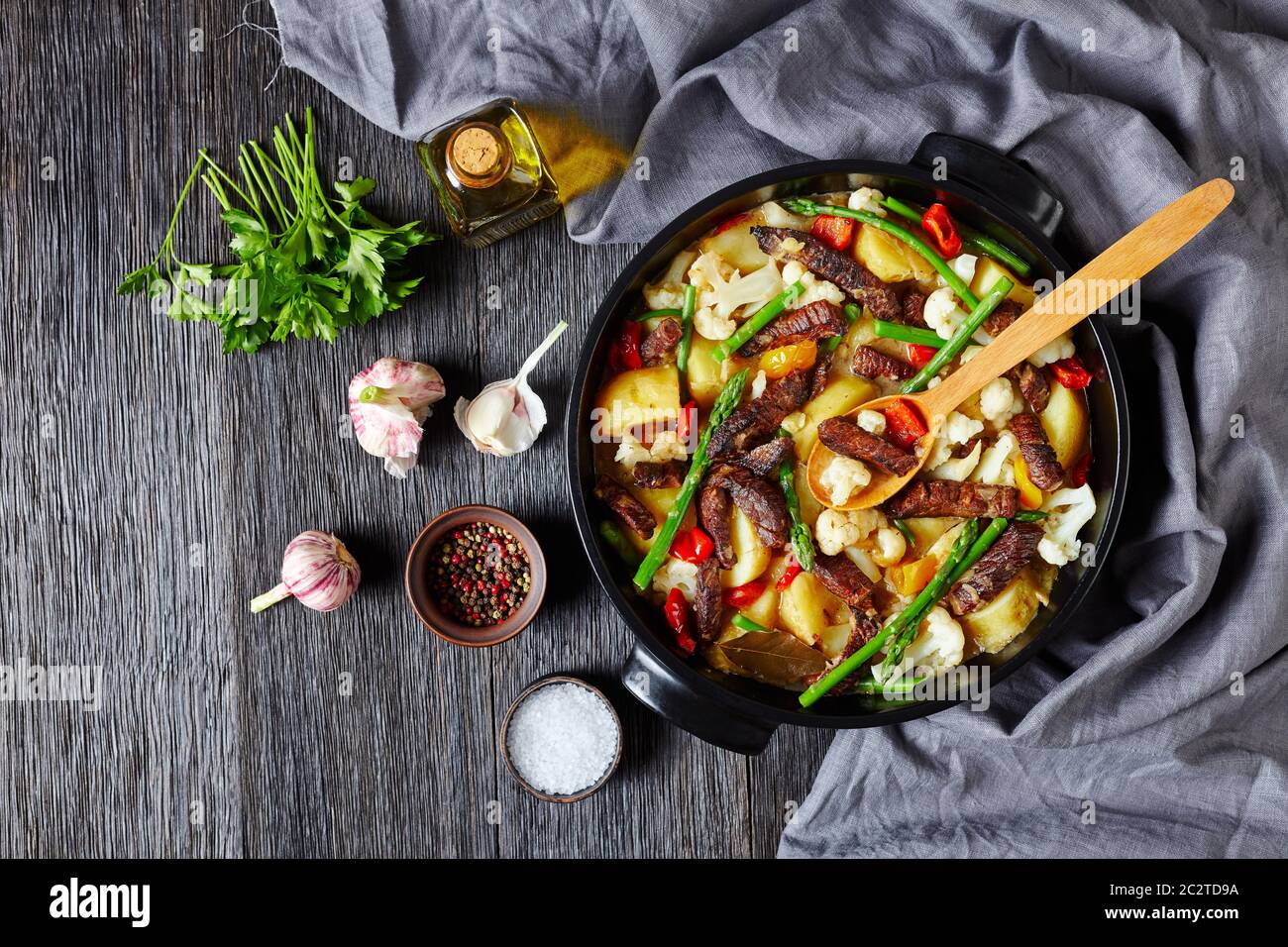 Ragoût de bœuf cuit lentement avec pommes de terre neuves, asperges et chou-fleur dans un four hollandais noir sur une table en bois, vue horizontale depuis le dessus, plat, gratuit Banque D'Images