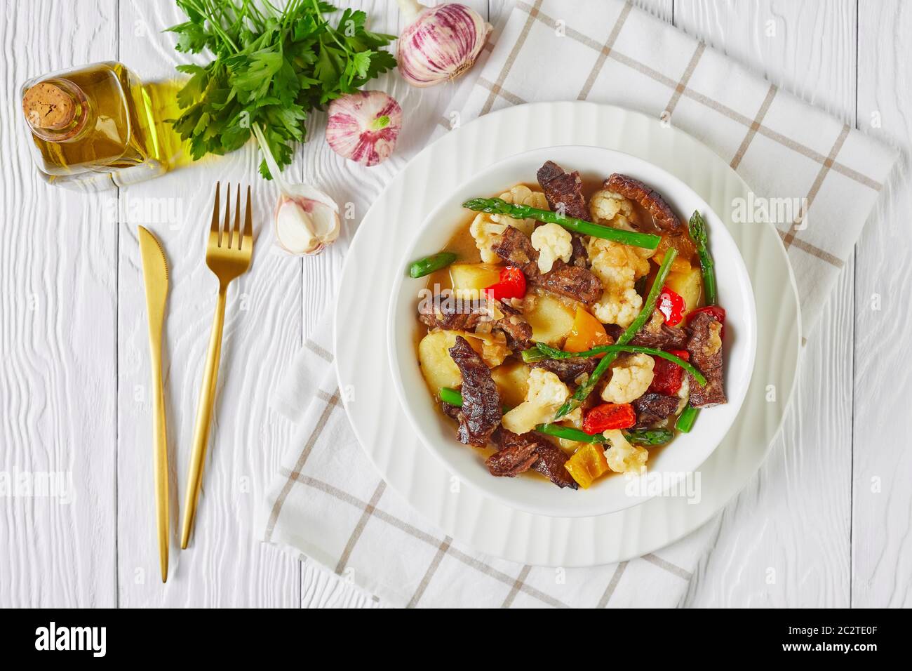 Gros plan de lanières de bœuf estival ragoût de pommes de terre neuves, asperges et chou-fleur dans un bol blanc sur une table en bois, cuisine américaine, vue sur le paysage, Banque D'Images