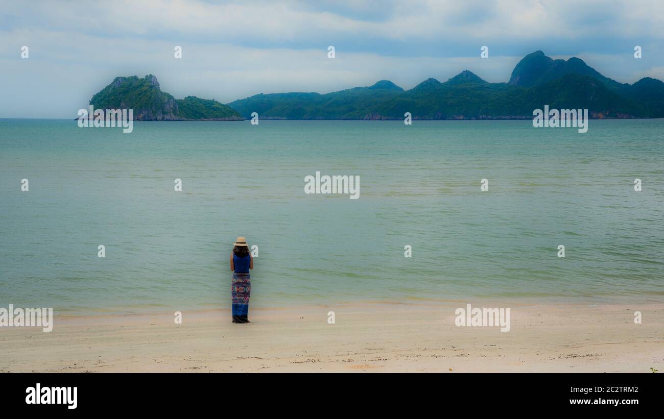 Femme en chapeau fedora blanc et sarong debout sur la plage avec des îles en arrière-plan à Khao Lommuak Thaïlande Banque D'Images