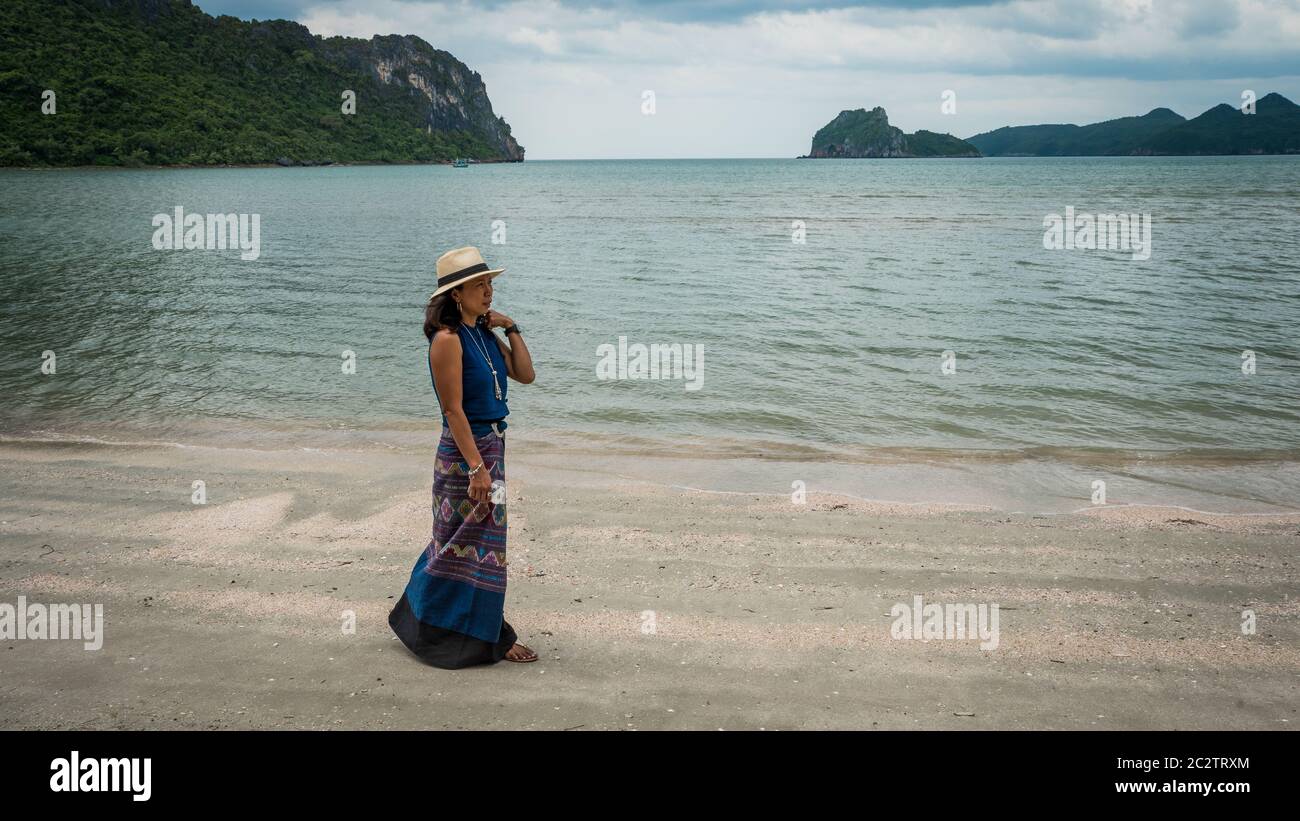Femme en chapeau fedora blanc et sarong debout sur la plage avec des îles en arrière-plan à Khao Lommuak Thaïlande Banque D'Images