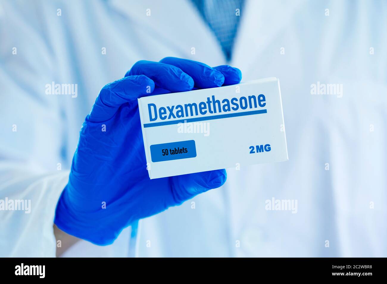 gros plan d'un homme, portant un manteau blanc et des gants chirurgicaux bleus, ayant une boîte simulée de dexaméthasone dans sa main Banque D'Images