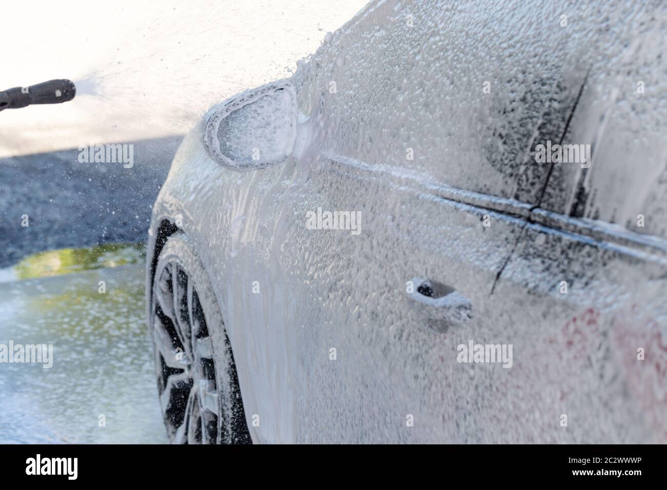 Gros plan du lavage manuel de la voiture, nettoyage avec de la mousse, eau sous pression. Lavage de voiture en libre-service avec tuyau haute pression Banque D'Images