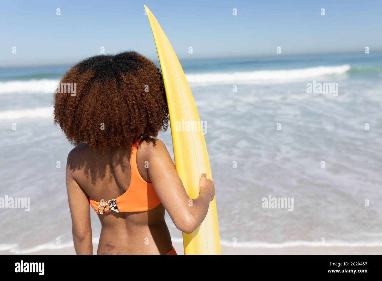 Femme de race mixte tenant une planche de surf sur la plage Banque D'Images