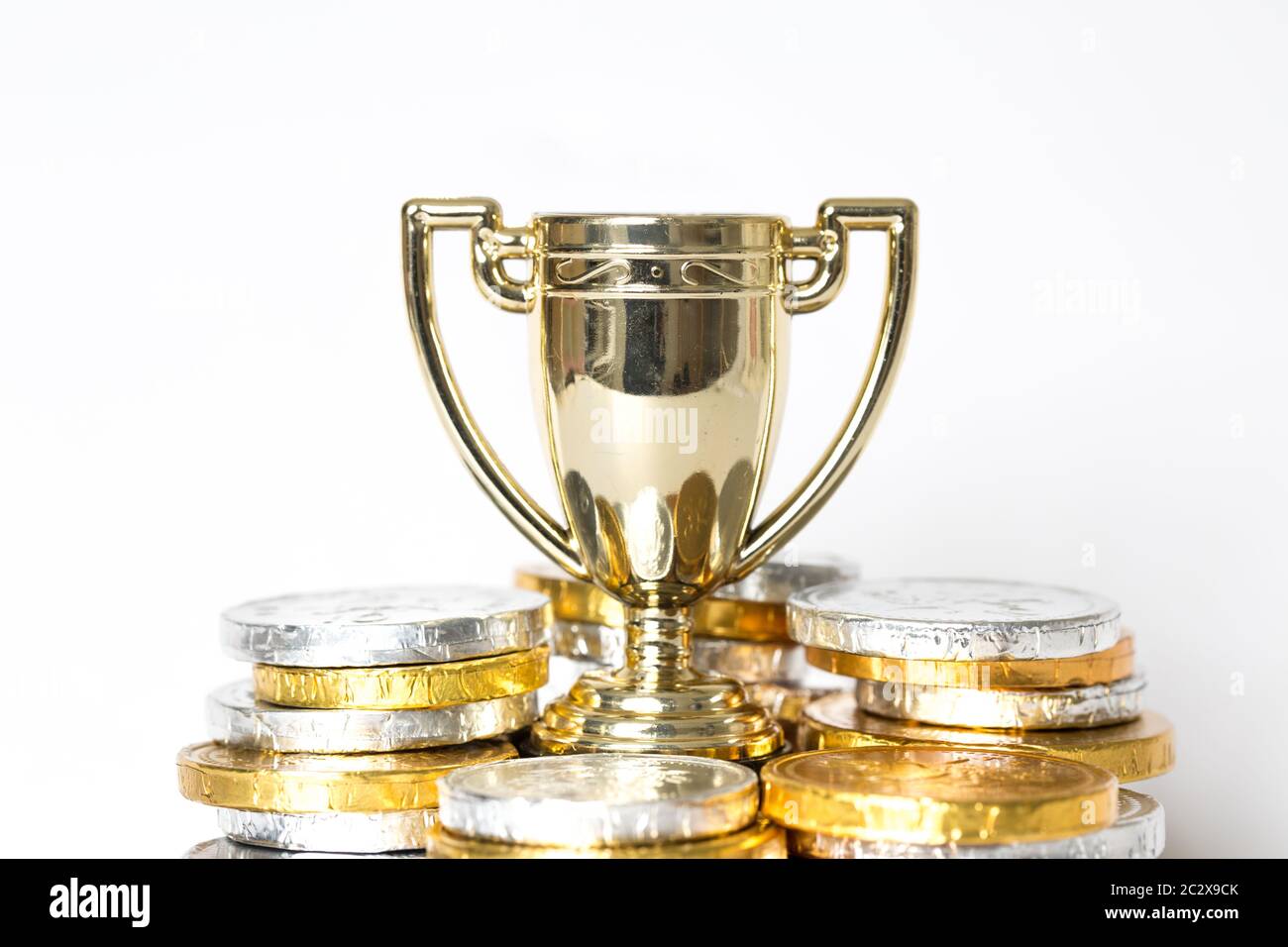 Un concept de réussite ou de victoire avec un trophée d'or ou une tasse entourée de pièces d'or et d'argent sous forme de prix Banque D'Images