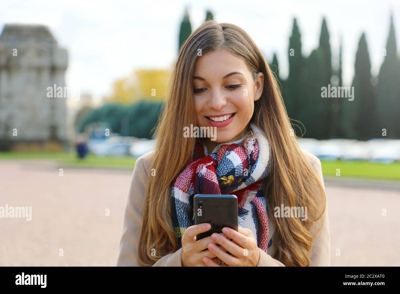 Jeune femme d'affaires à taper un message sur téléphone mobile walking in city street portant manteau et foulard en hiver. Banque D'Images