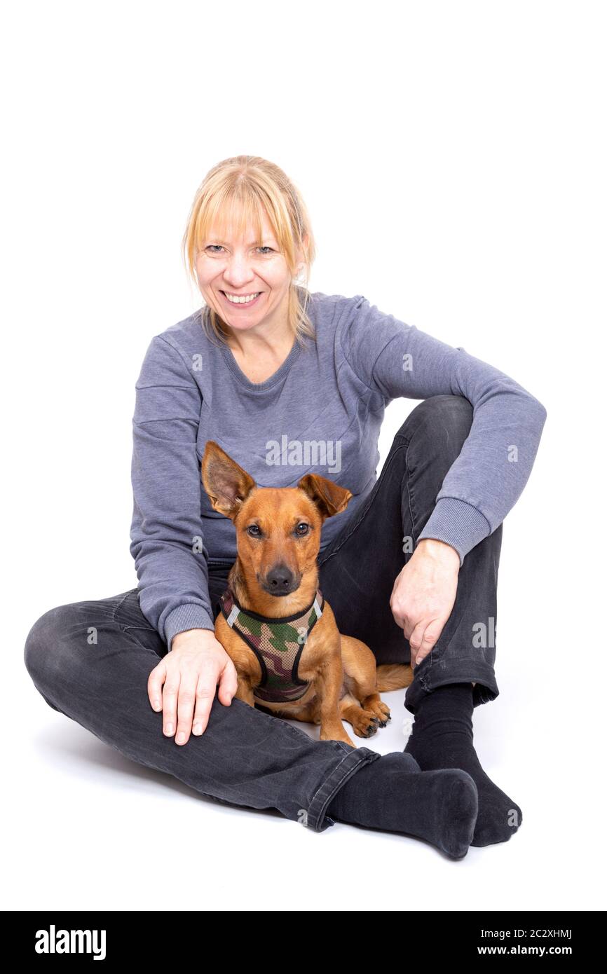 Femme blonde assise sur le sol avec son petit chien brun isolé sur fond blanc dans le studio. Petite race mixte de cric Banque D'Images