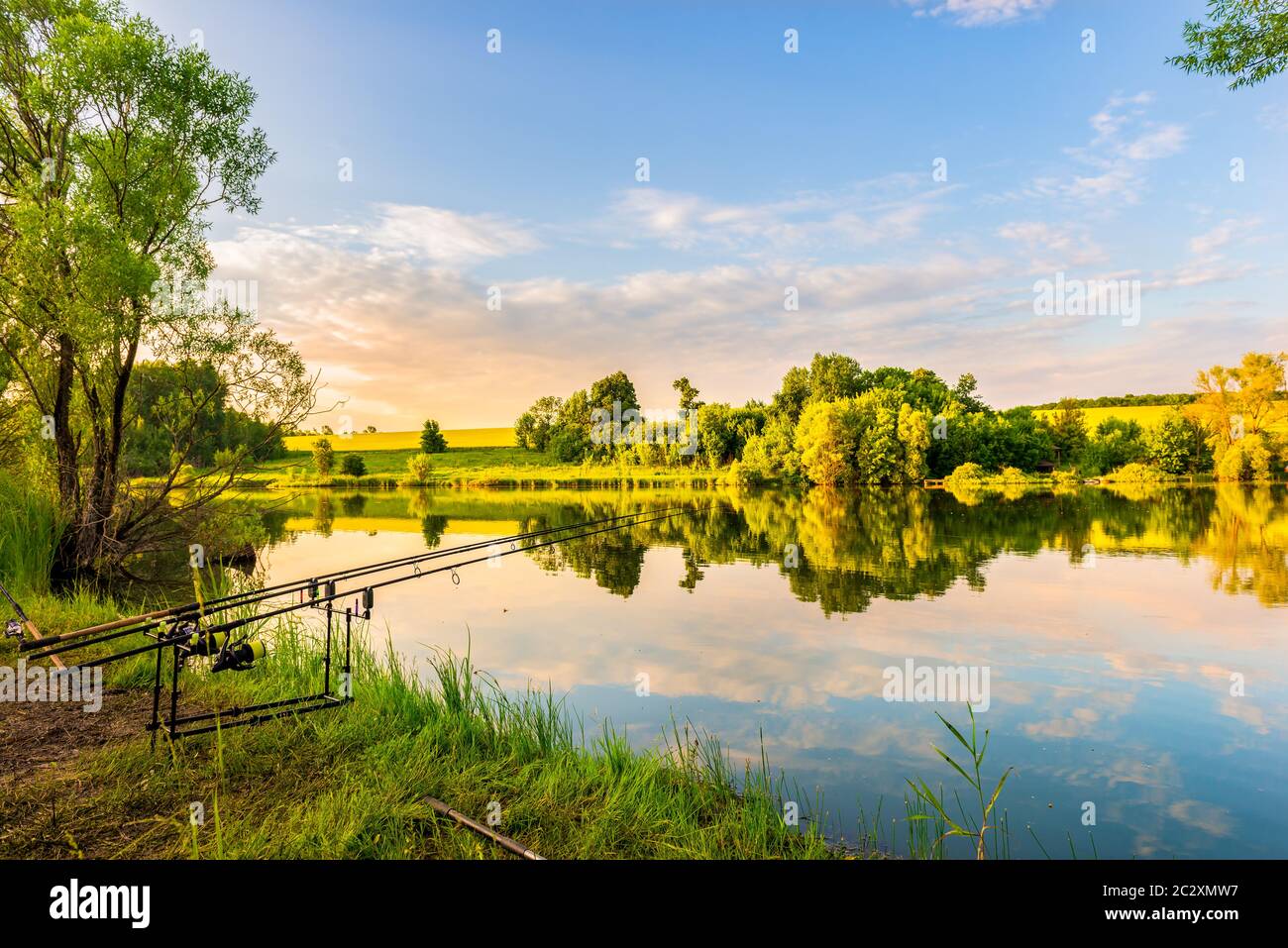 Des cannes de pêche sur une rive de rivière calme au coucher du soleil Banque D'Images