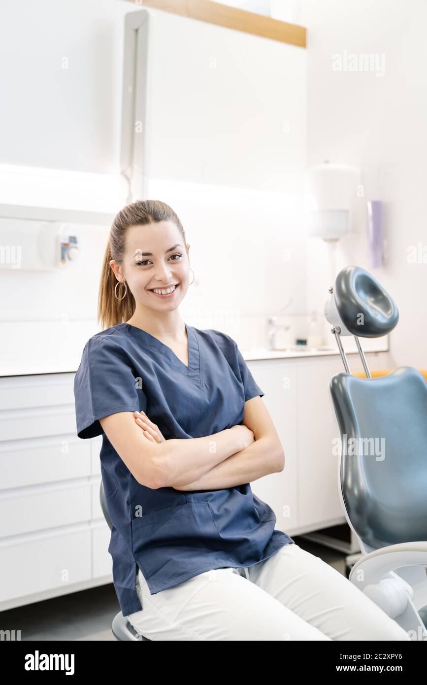 Une jeune infirmière en blouson bleu sourit dans le cabinet dentaire avant de recevoir le patient Banque D'Images