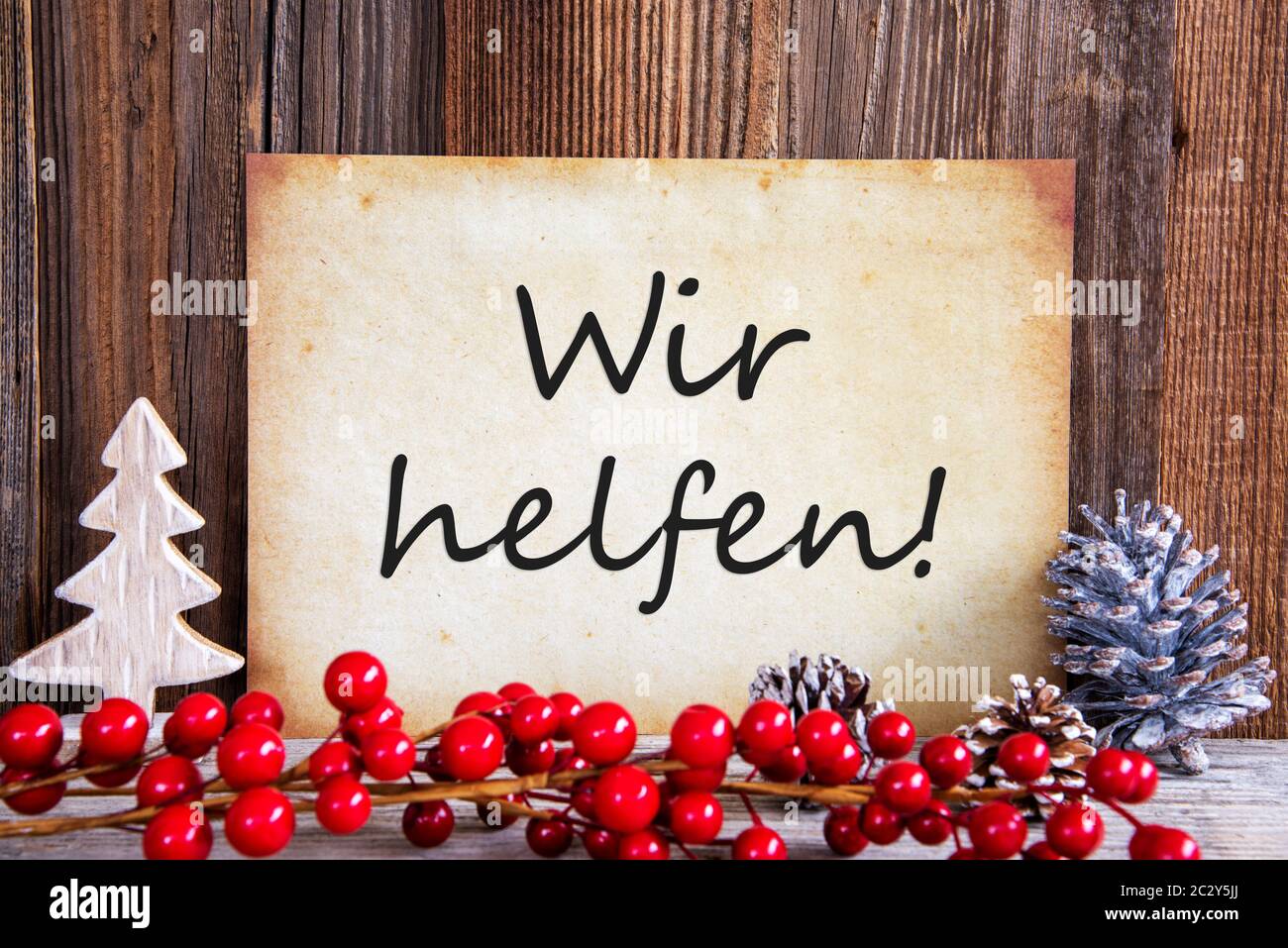 Papier avec texte allemand Wir helfen signifie que nous aider. Décoration de Noël et de fond de bois Banque D'Images