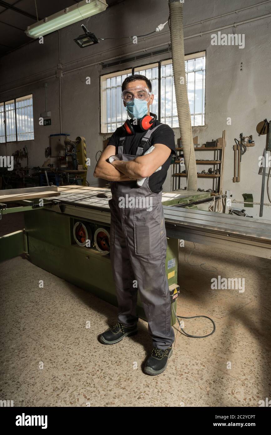 Travailleur debout portant un masque et un équipement de protection regardant la caméra dans une usine. Photo longue, corps entier. Banque D'Images