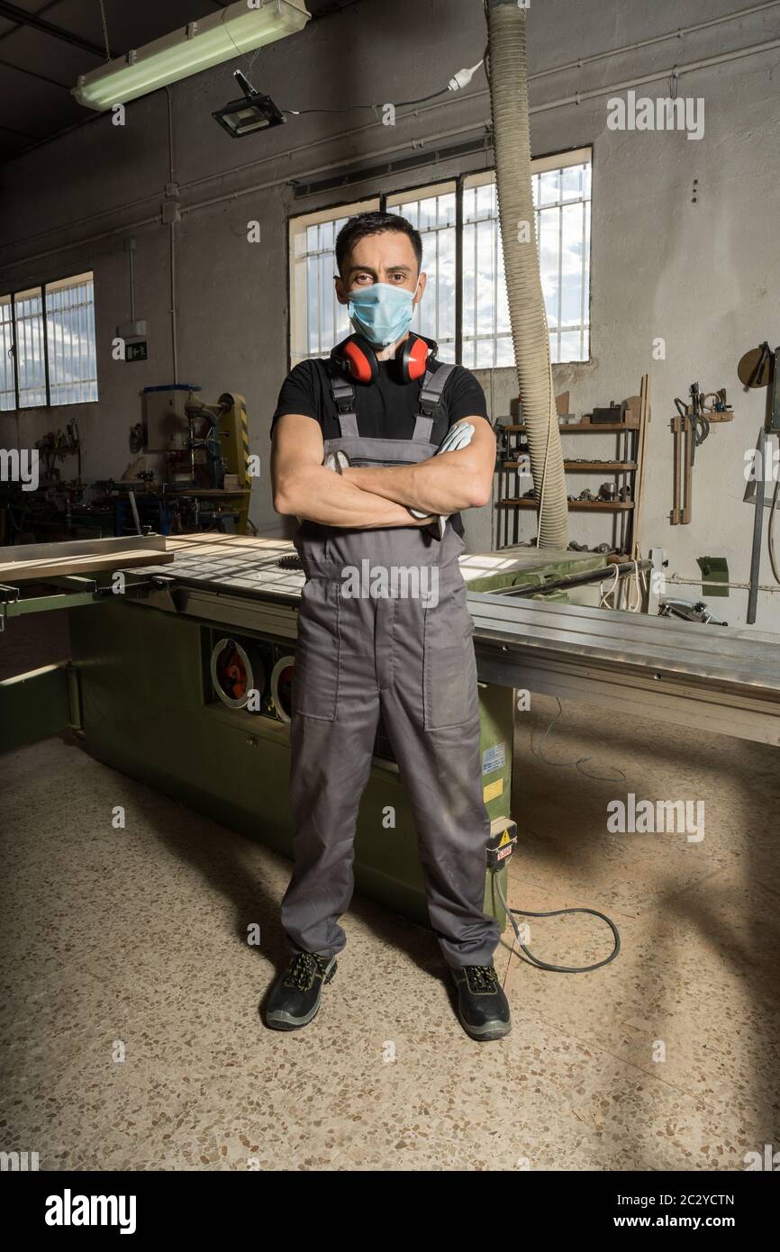 Travailleur debout portant un masque et un équipement de protection regardant la caméra dans une usine. Photo longue, corps entier. Banque D'Images