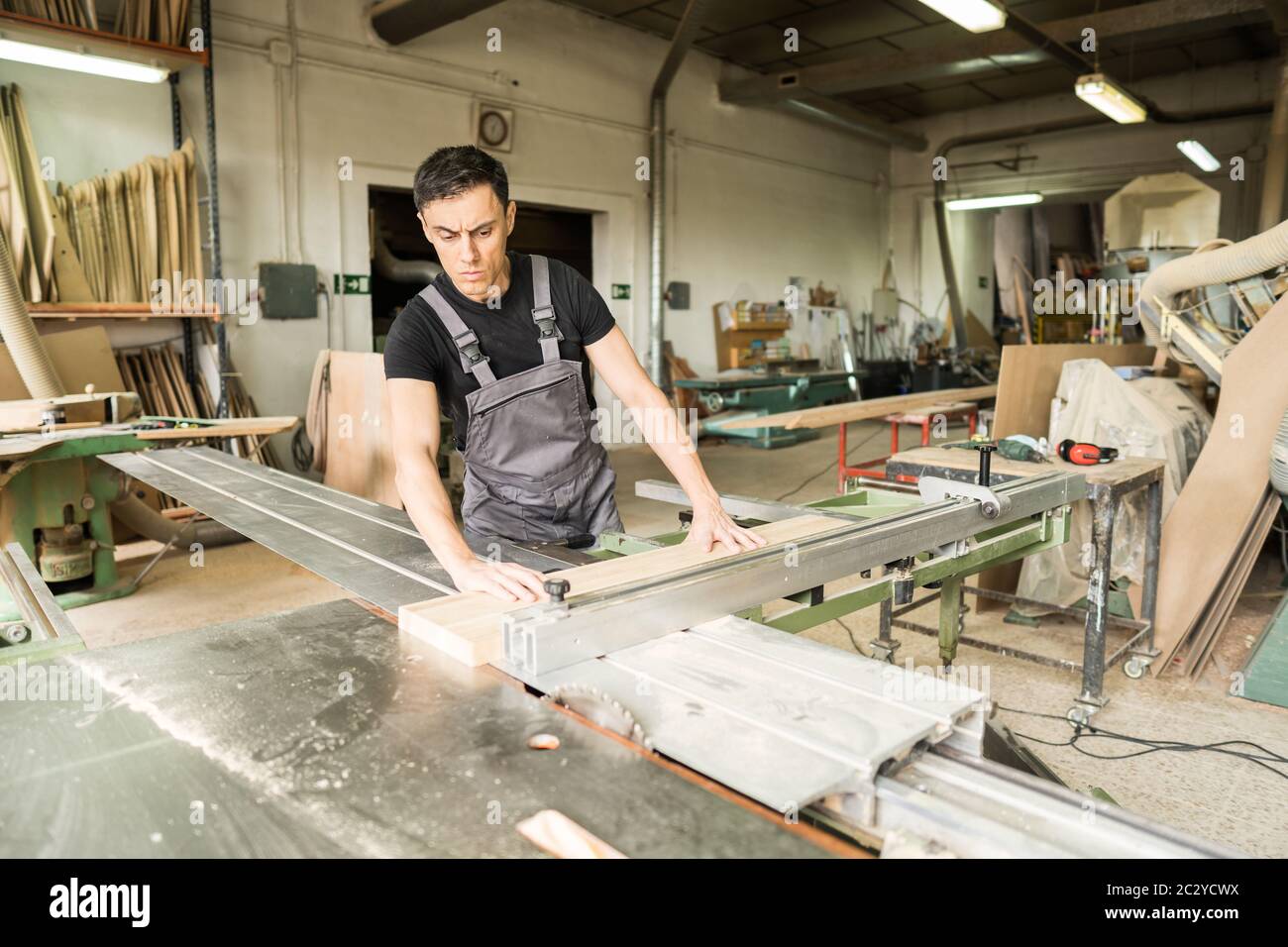 Un travailleur qui coupe sur une scie à table coulissante en usine. Photo intermédiaire. Banque D'Images