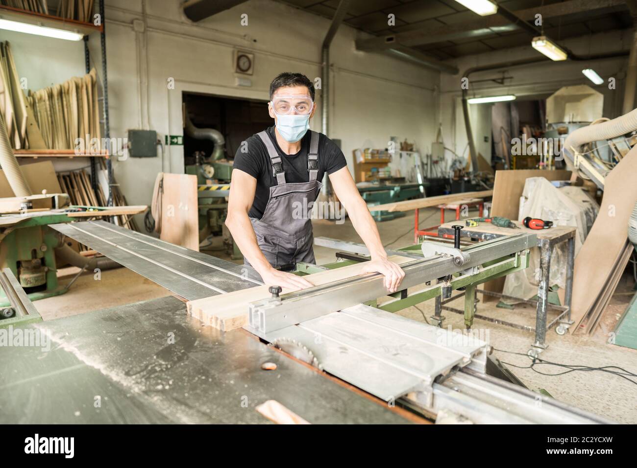 Travailleur avec masque et équipement de protection coupant sur une scie à table coulissante en usine. Photo intermédiaire. Banque D'Images