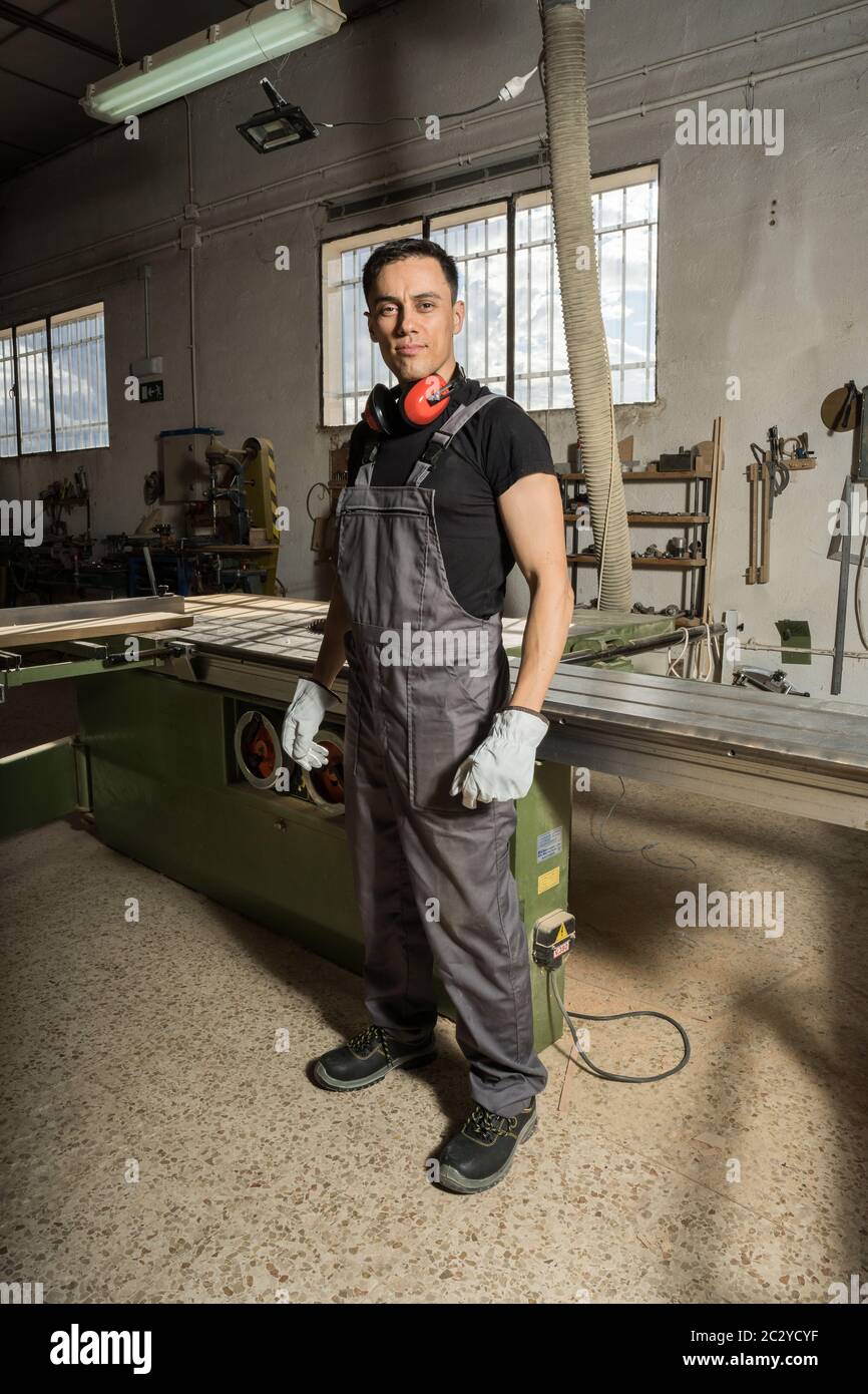 Travailleur debout avec un équipement de protection regardant la caméra sourire dans une usine. Photo longue, corps entier. Banque D'Images