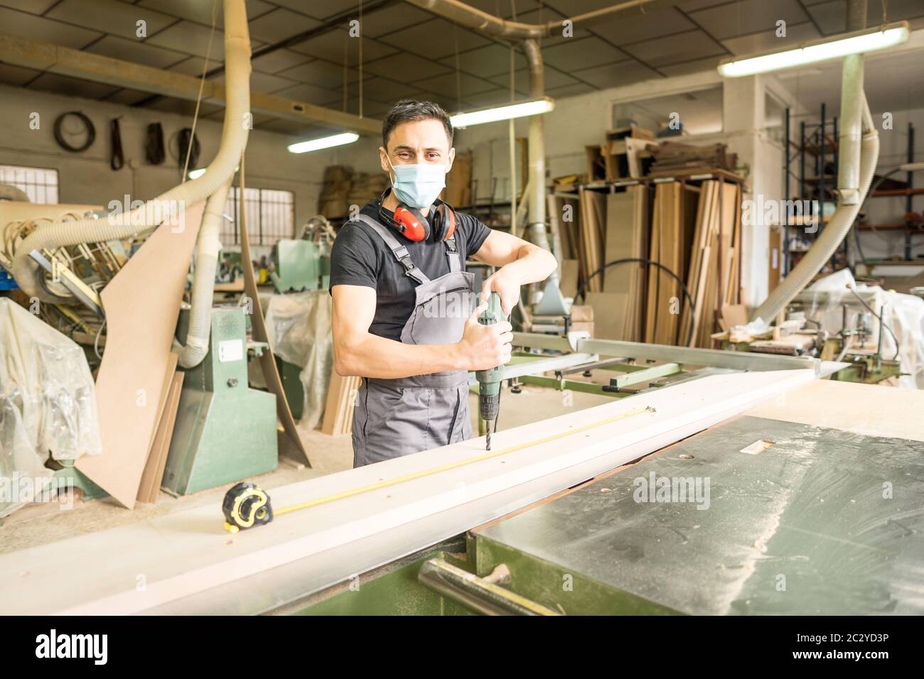 Travailleur debout avec un masque et un équipement de protection travaillant avec un semoir dans une usine. Photo intermédiaire. Banque D'Images