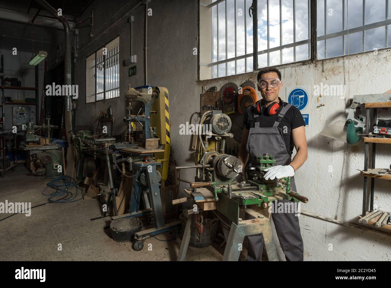 Travailleur debout avec un équipement de protection regardant la caméra sourire dans une usine. Photo intermédiaire. Banque D'Images