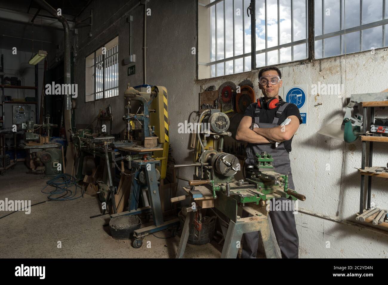 Travailleur debout avec un équipement de protection regardant la caméra sourire dans une usine. Photo intermédiaire. Banque D'Images