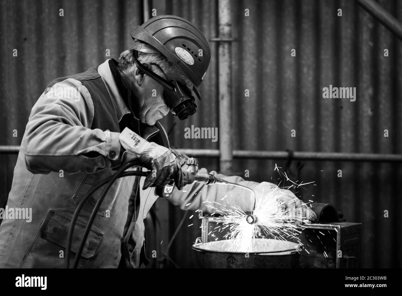 Un mécanicien avec casque de sécurité fait des autogènes coupant un tuyau avec une flamme d'acétylène et d'oxygène. Des étincelles sont émises par le matériau. Banque D'Images