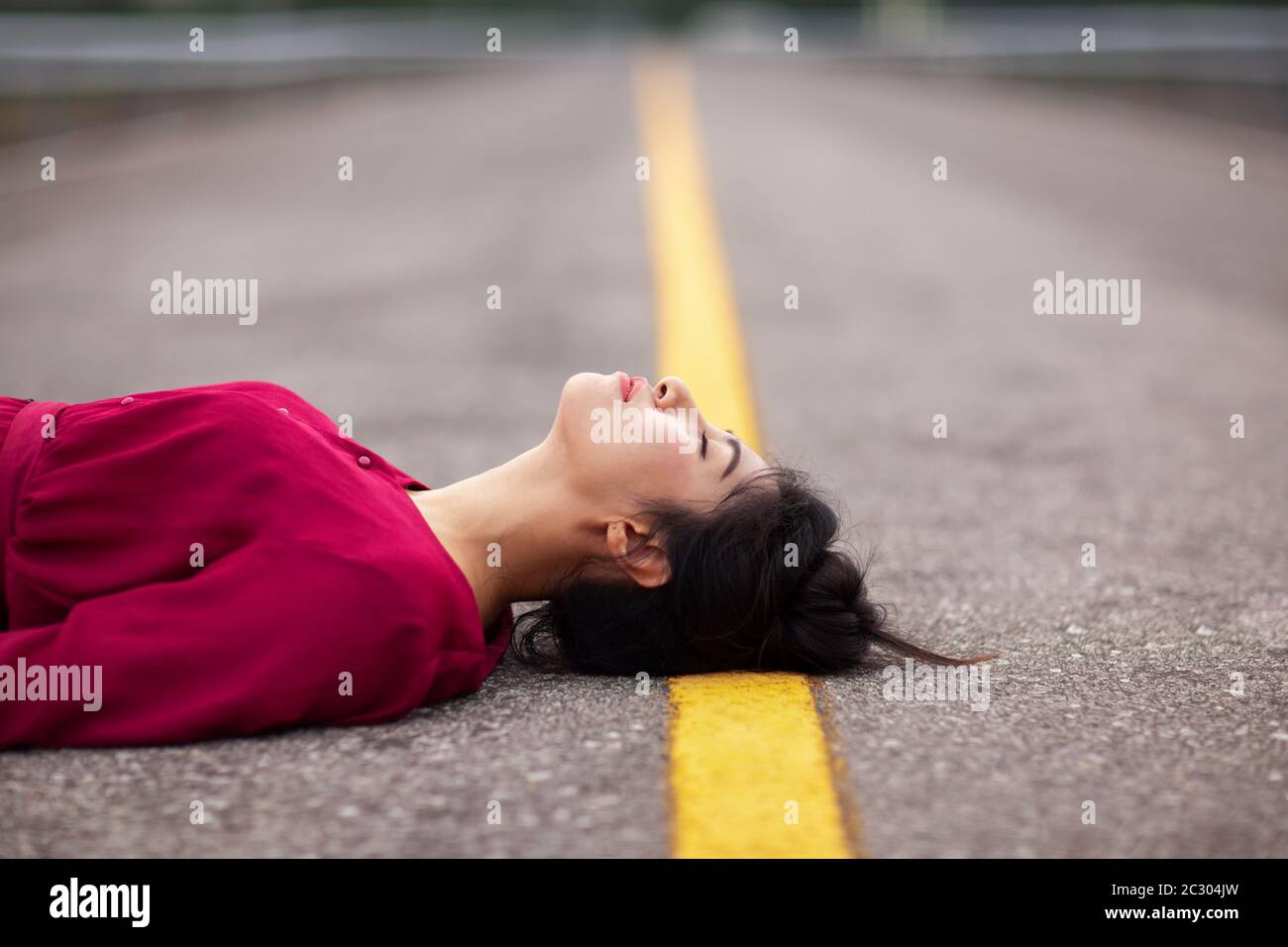 Portrait of beautiful young asian woman dans Carmen robe rouge couché sur la route jaune de ligne vide, à l'intérieur du parc public Banque D'Images