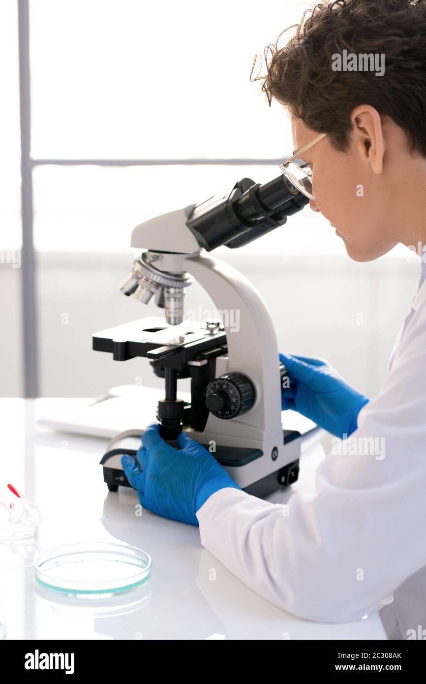 Vue sur l'épaule d'un chercheur de laboratoire concentré utilisant un microscope tout en travaillant avec des échantillons médicaux en laboratoire Banque D'Images
