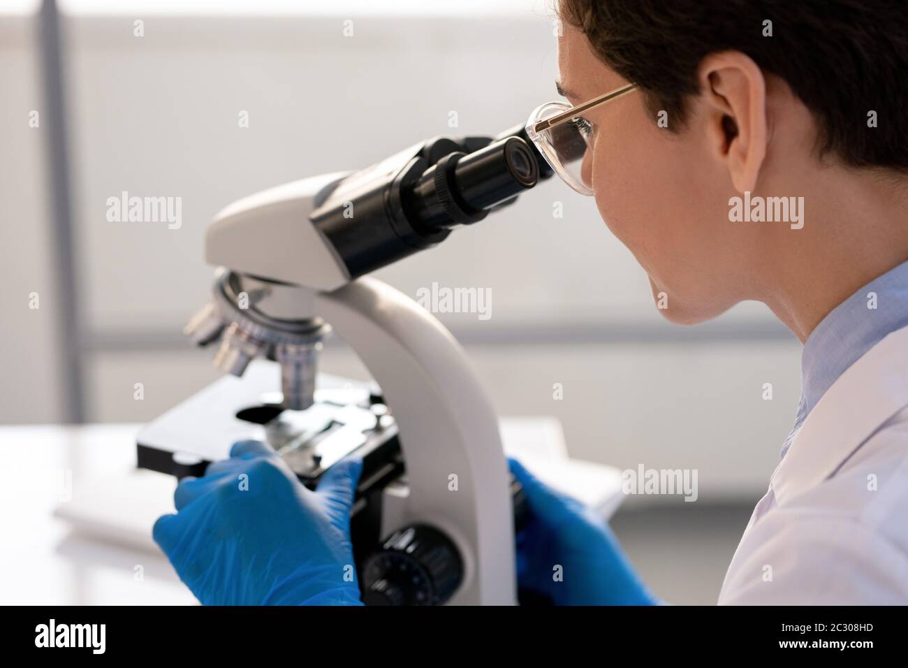 Travailleur de laboratoire concentré dans des gants utilisant un microscope lors de l'analyse de la structure cellulaire Banque D'Images