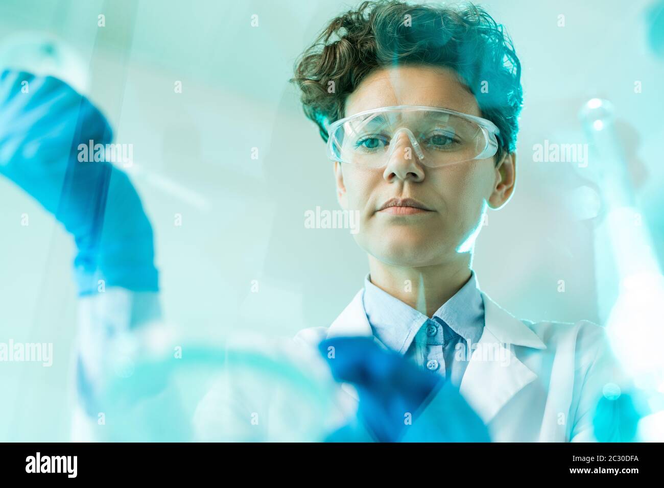 Vue ci-dessous de la chercheuse concentrée dans les lunettes de sécurité travaillant avec des échantillons en laboratoire Banque D'Images