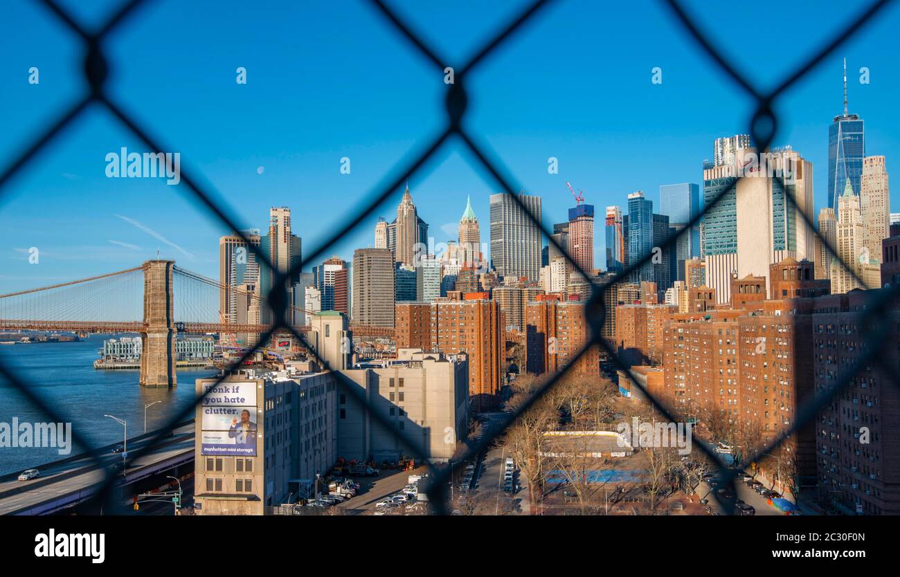 Vue depuis le pont de Manhattan à travers la clôture en treillis métallique sur la rivière East jusqu'à la ligne d'horizon de Lower Manhattan et du pont de Brooklyn, Manhattan, New York, États-Unis Banque D'Images