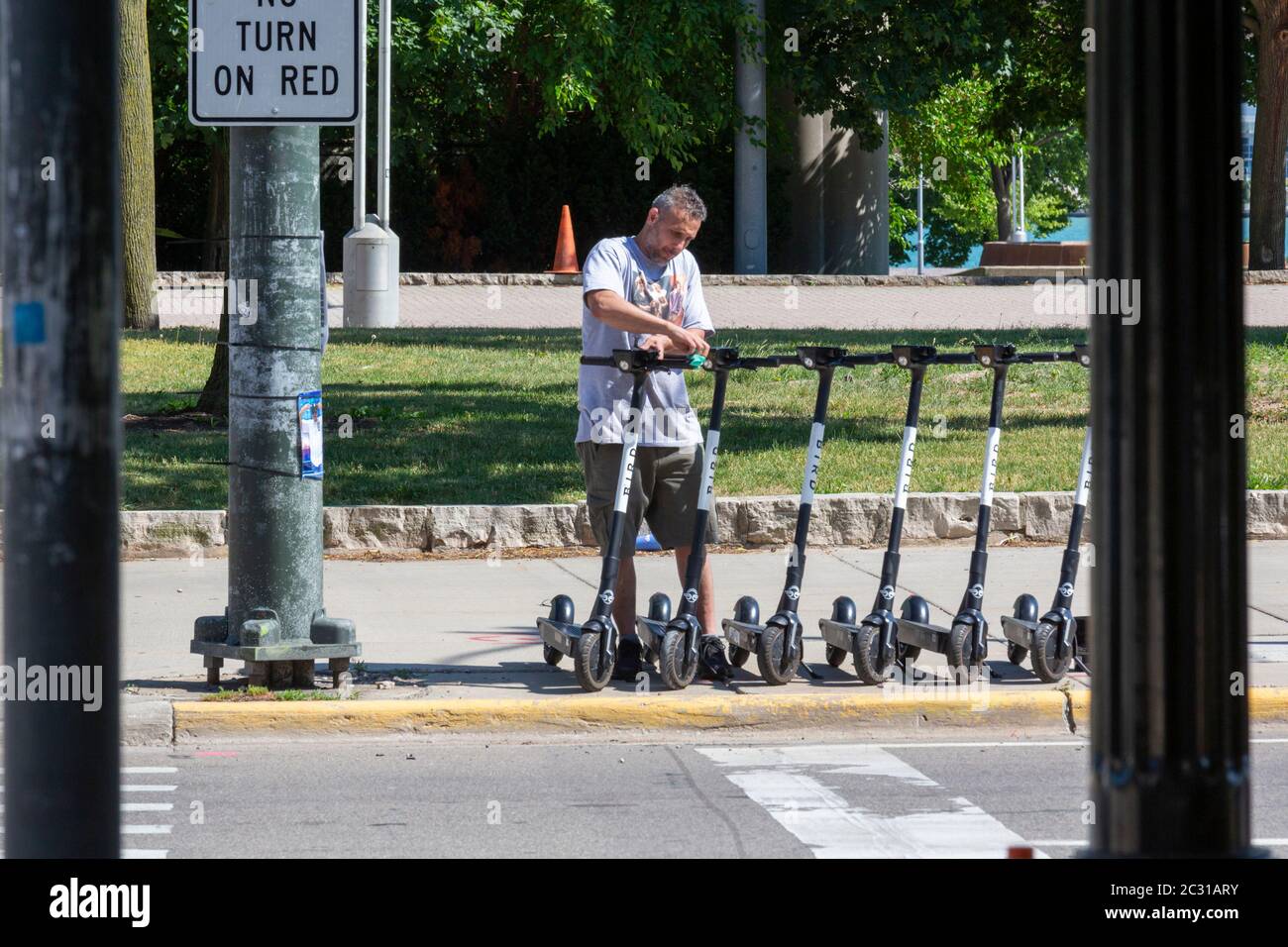 Detroit, Michigan - UN travailleur utilise des lingettes désinfectantes pour désinfecter les scooters électriques partagés garés dans une rue urbaine pendant la pandémie du coronavirus. Banque D'Images