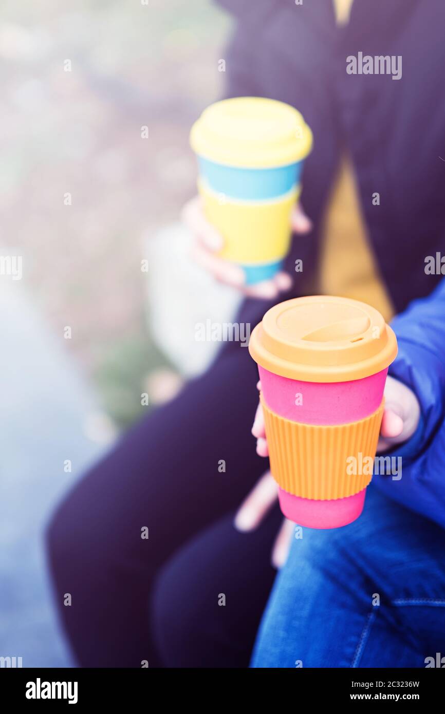 Deux femmes assises à l'extérieur avec des tasses de café en bambou réutilisables dans leurs mains. Aucun gaspillage. Concept de mode de vie durable. Banque D'Images