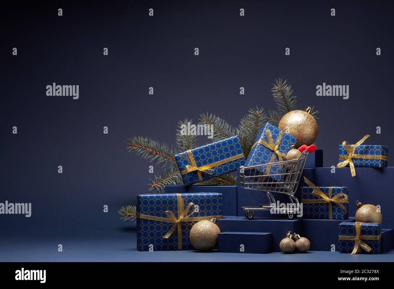 Chariot à provisions, boîtes-cadeaux, branches en sapin et décorations de Noël sur fond bleu foncé avec espace pour les copies. Noël et nouvel an. SAL. Hiver Banque D'Images