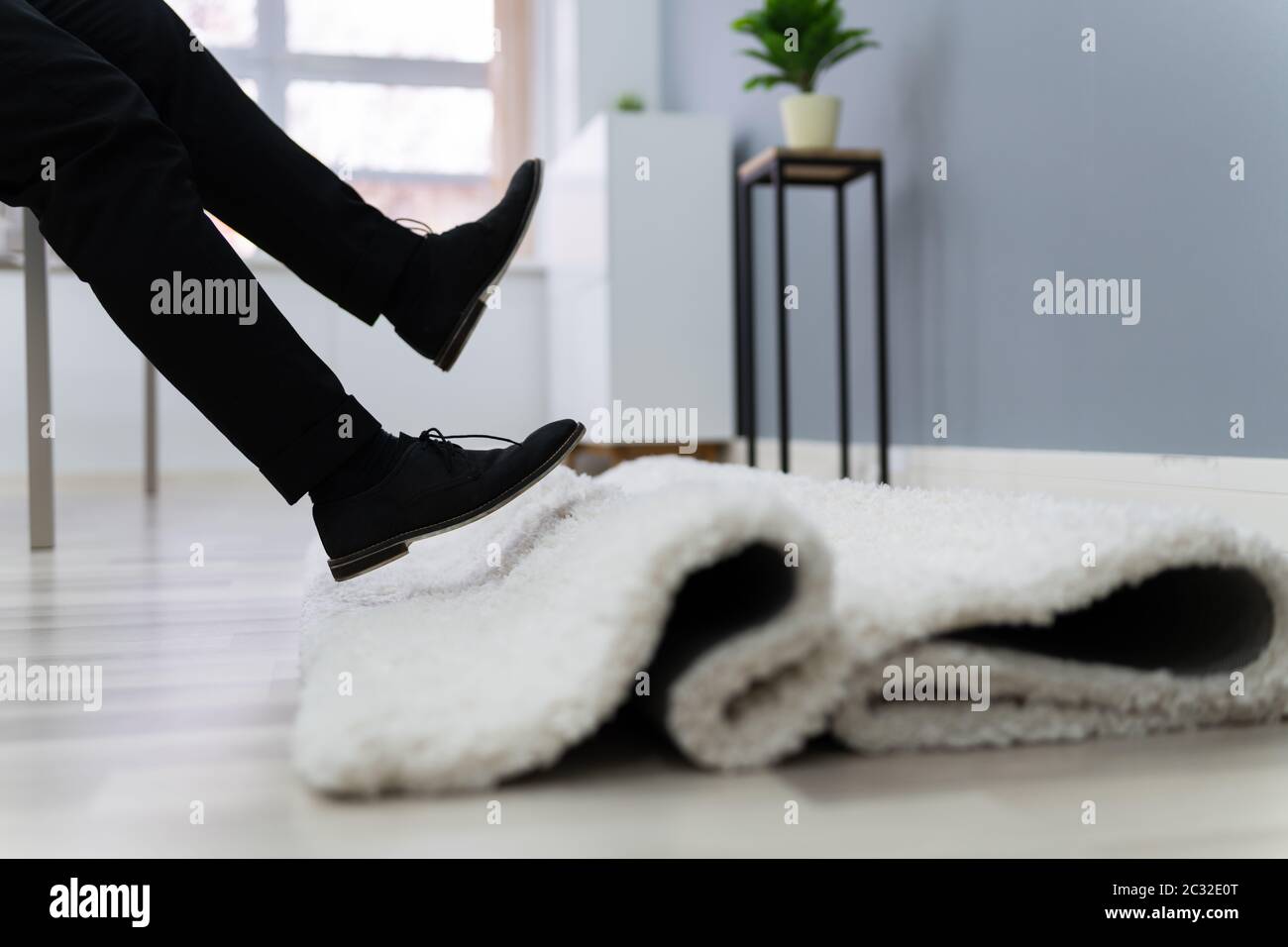 La section basse de l'homme aux jambes d'achoppement d'un tapis dans la salle de séjour à la maison Banque D'Images