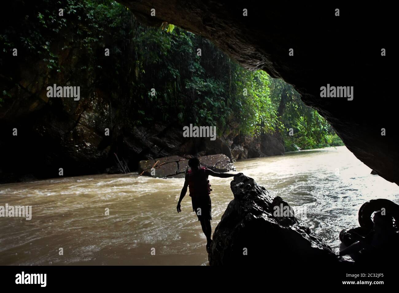 Un guide aventure se déplaçant sur la sortie rocheuse de la grotte de Kalong (Bat) pour commencer l'activité de tubing de rivière lors d'un jour pluvieux à Tangkahan, Sumatra, Indonésie. Banque D'Images