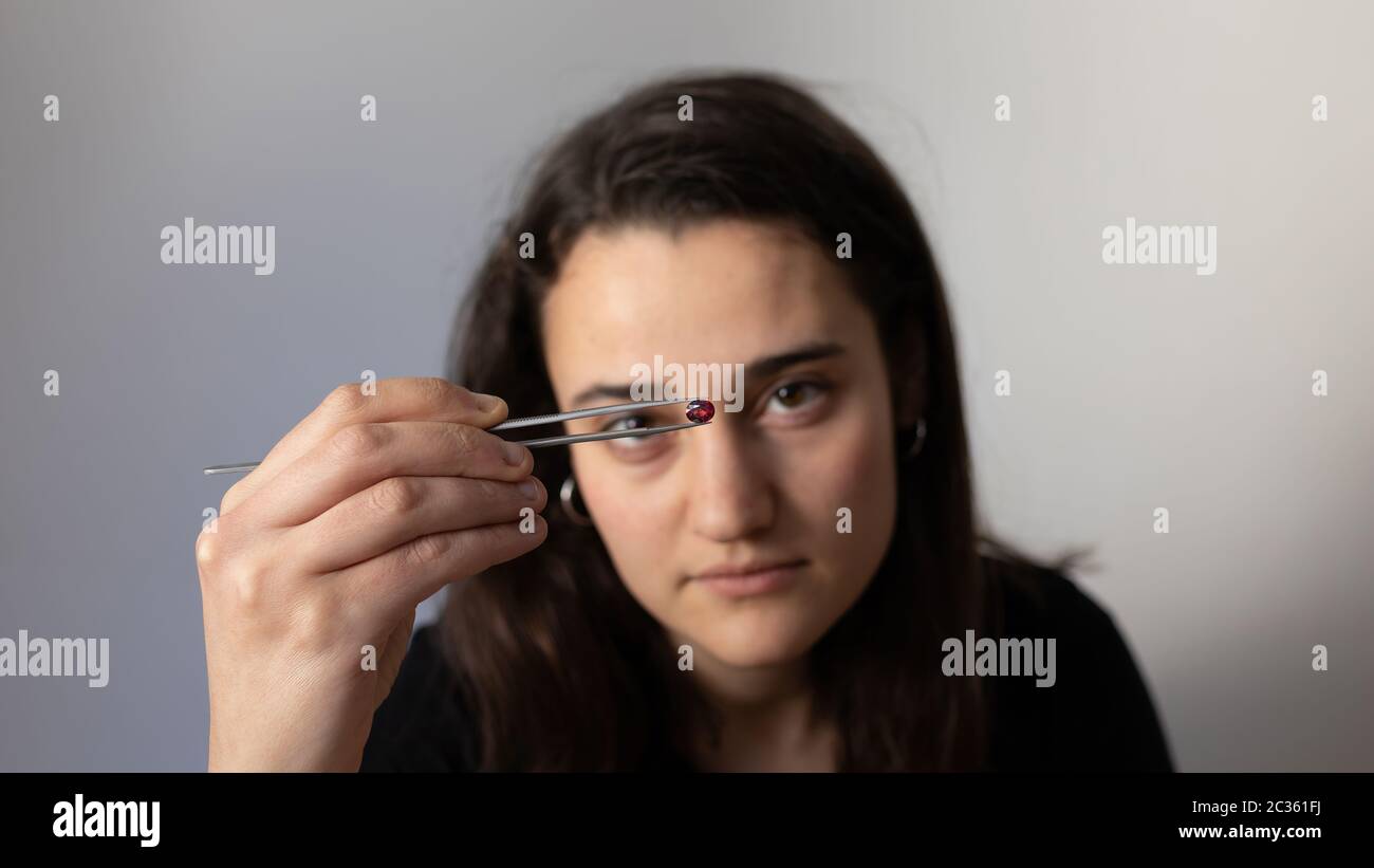 Jeune femme tenant une pierre précieuse avec des pinces à bijoux. Portrait d'un gemmologue. Banque D'Images