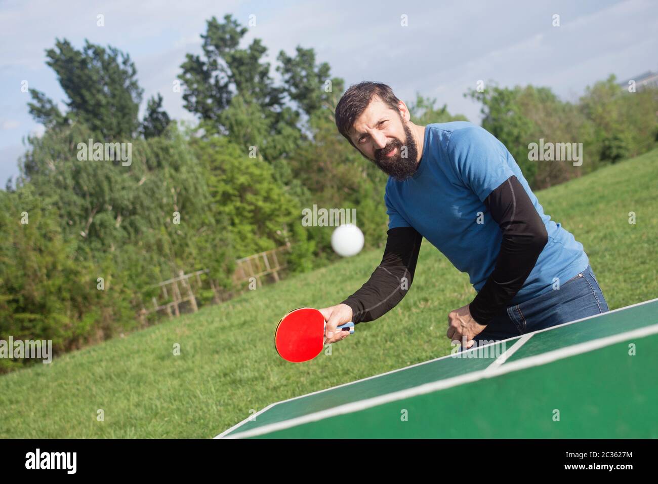 L'homme barbu joue au tennis de table en plein air, concept de vie active. Banque D'Images