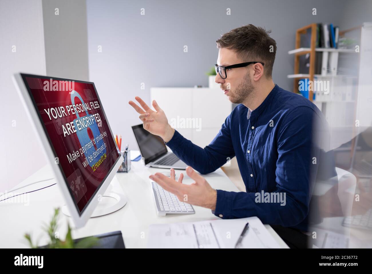 Inquiets Businessman Looking At Computer avec Ransomware mots à l'écran sur le lieu de travail Banque D'Images