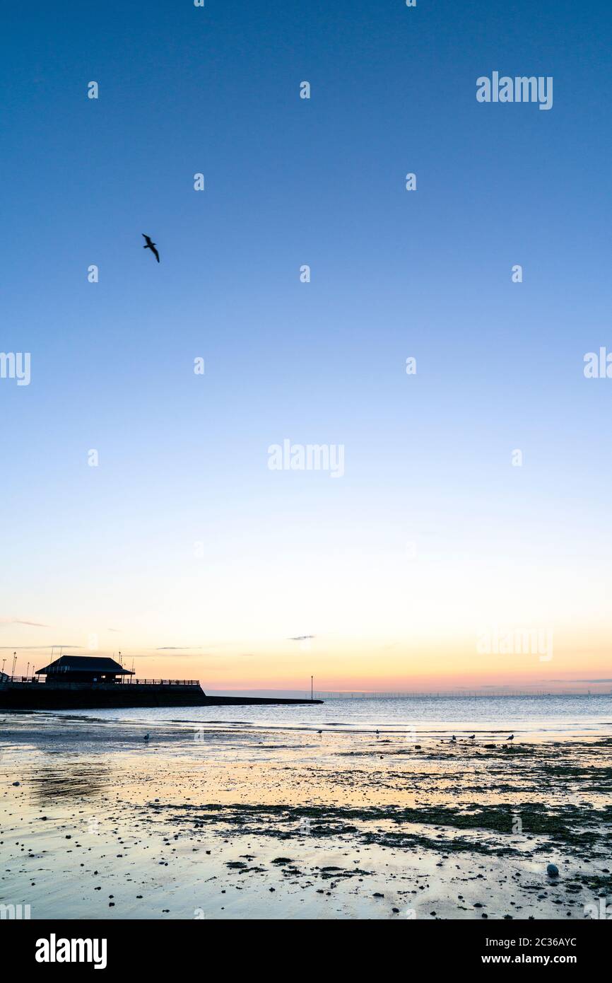 Le ciel de l'aube au-dessus de la plage de Viking Bay et du port de Broadescaliers avec la marée dehors. Bande de ciel orange à l'horizon se tournant vers jaune puis au-dessus d'un ciel bleu clair. Vue en angle bas sur la mer. Banque D'Images