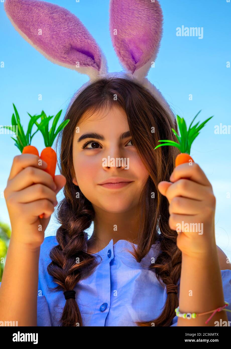 Portrait d'une jolie jeune fille de pré-adolescence célébrant de joyeuses vacances chrétiennes, vêtue d'un lapin de Pâques tenant des carottes, jardinage dans la cour Banque D'Images