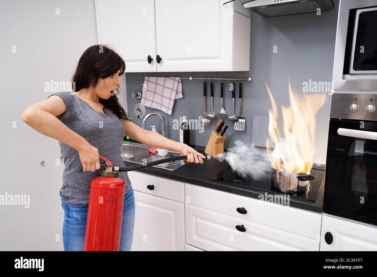 Femme à l'aide d'extincteur pour feu stop sur la gravure de casserole dans la cuisine Banque D'Images