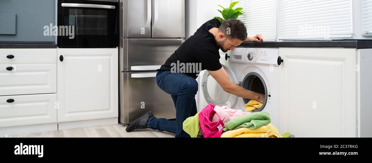 Homme chargeant des vêtements dans un lave-linge dans la cuisine Banque D'Images