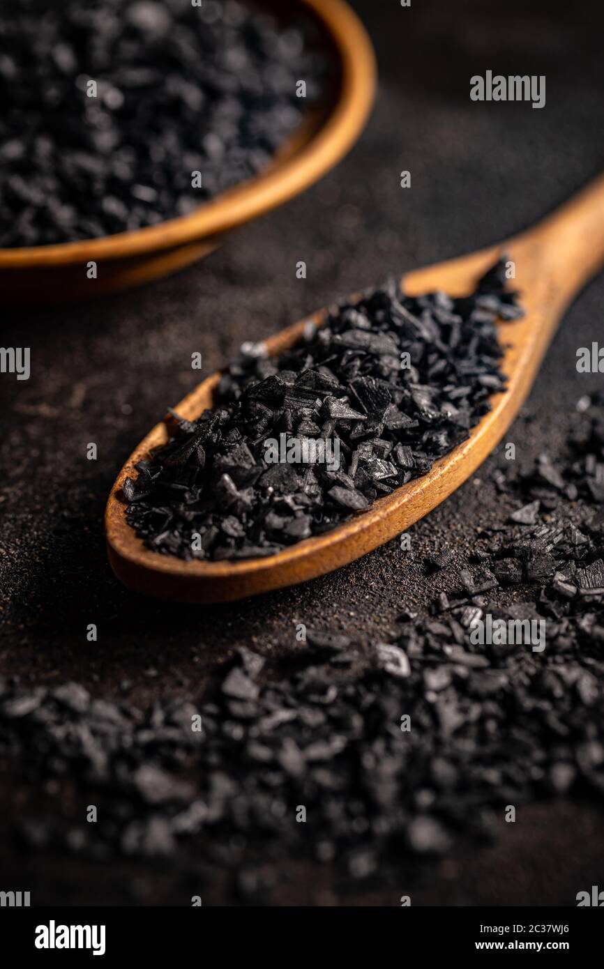 Gros plan de cristaux de sel noir dans une cuillère en bois sur fond noir Banque D'Images