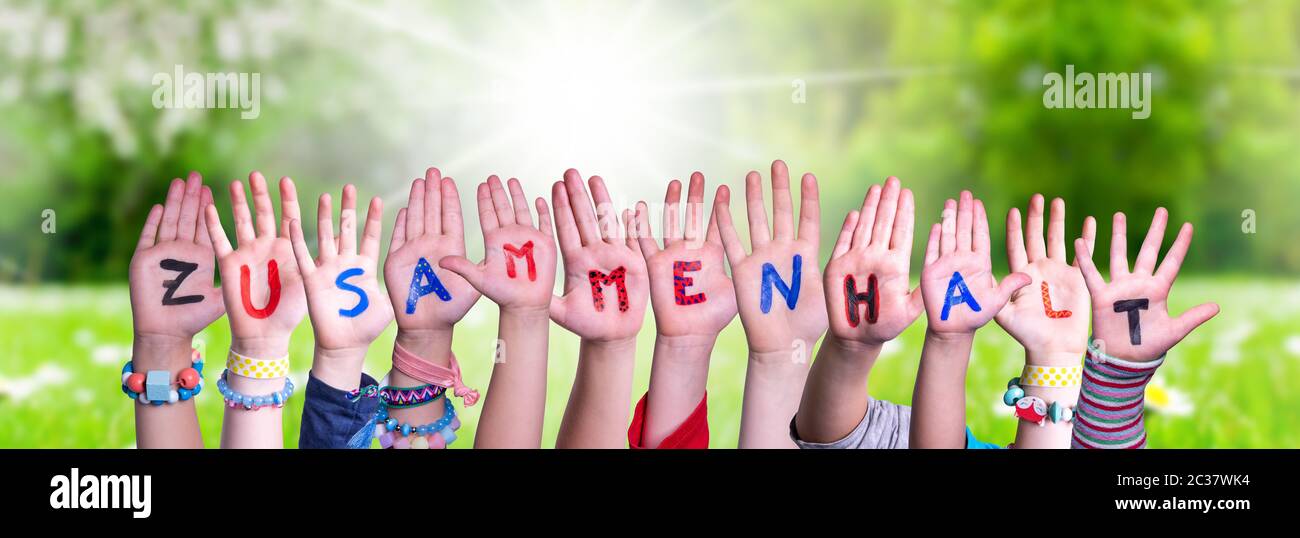 Les mains des enfants tenant le mot allemand coloré Zusammenhalt signifie la convivialité. Vert prairie ensoleillé comme arrière-plan Banque D'Images