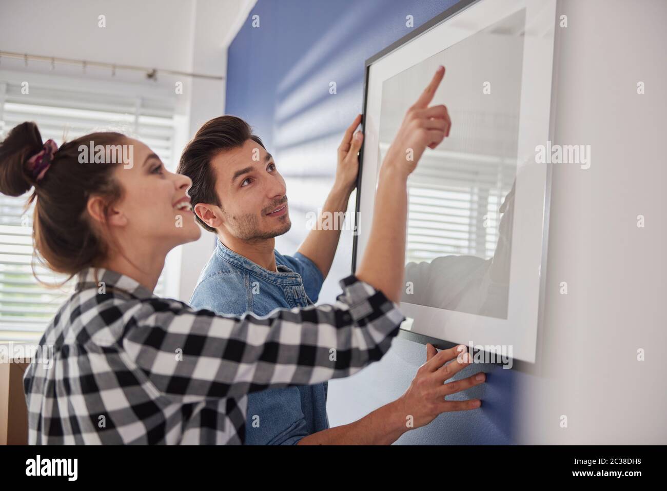 Femme aidant son petit ami à accrocher une image de cadre Banque D'Images